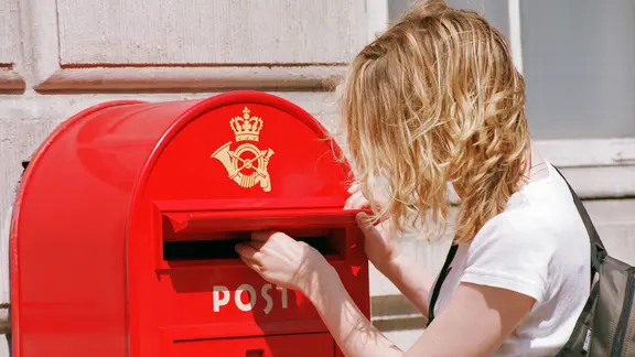 Eine Frau steckt einen Brief in einen roten Briefkasten.