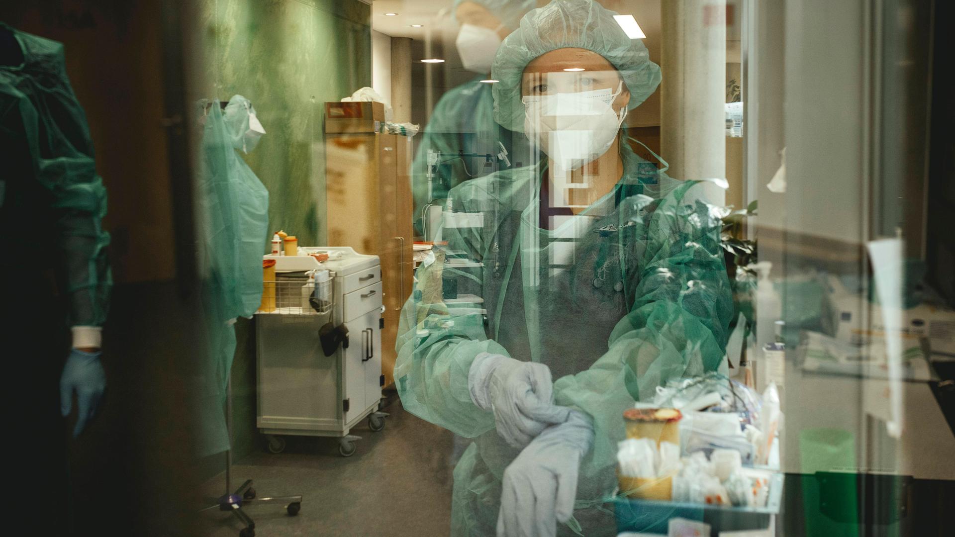 Ärzte vor Betreten der Covid-Station. Sie tragen Schutzkleidung und ziehen sich Handschuhe an.