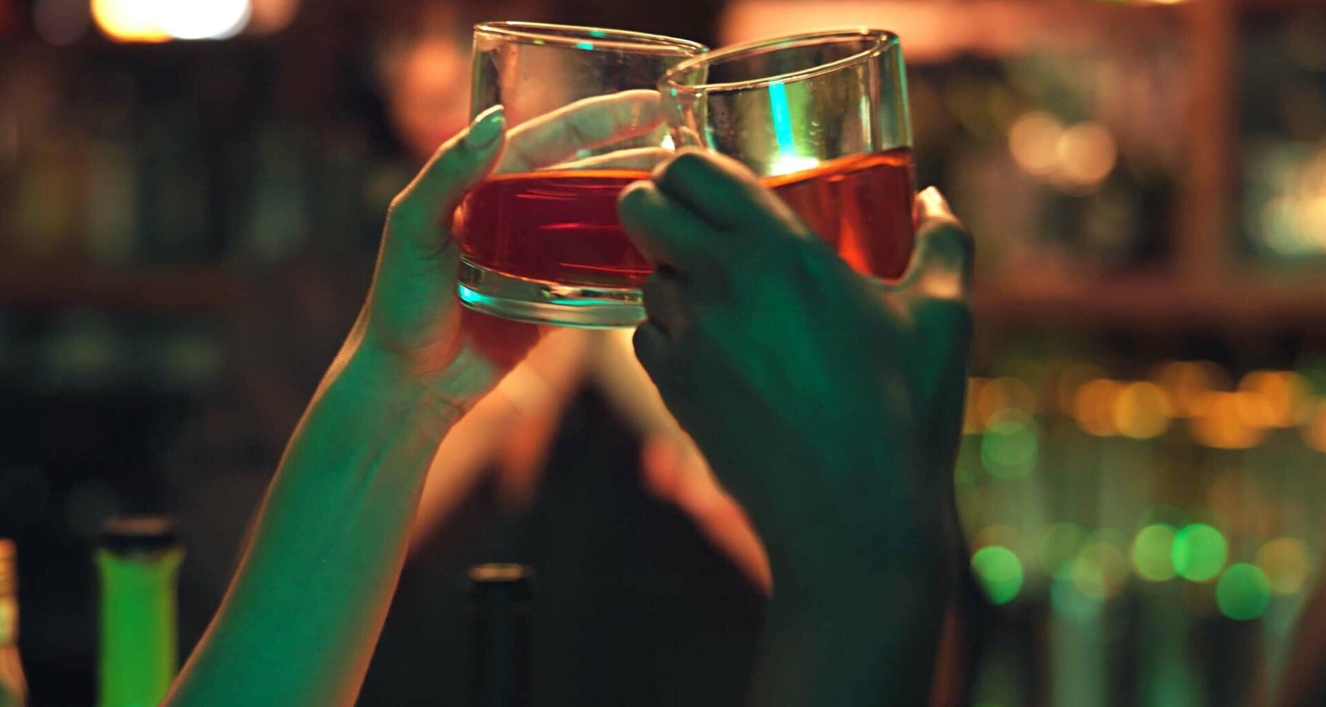 Zwei Personen stoßen mit einem Getränk in einer Bar an