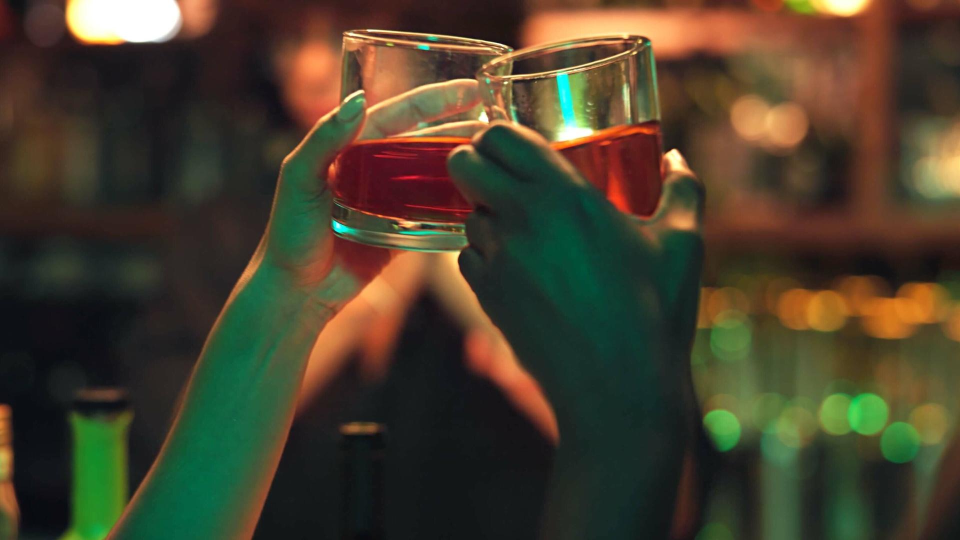Zwei Personen stoßen mit einem Getränk in einer Bar an