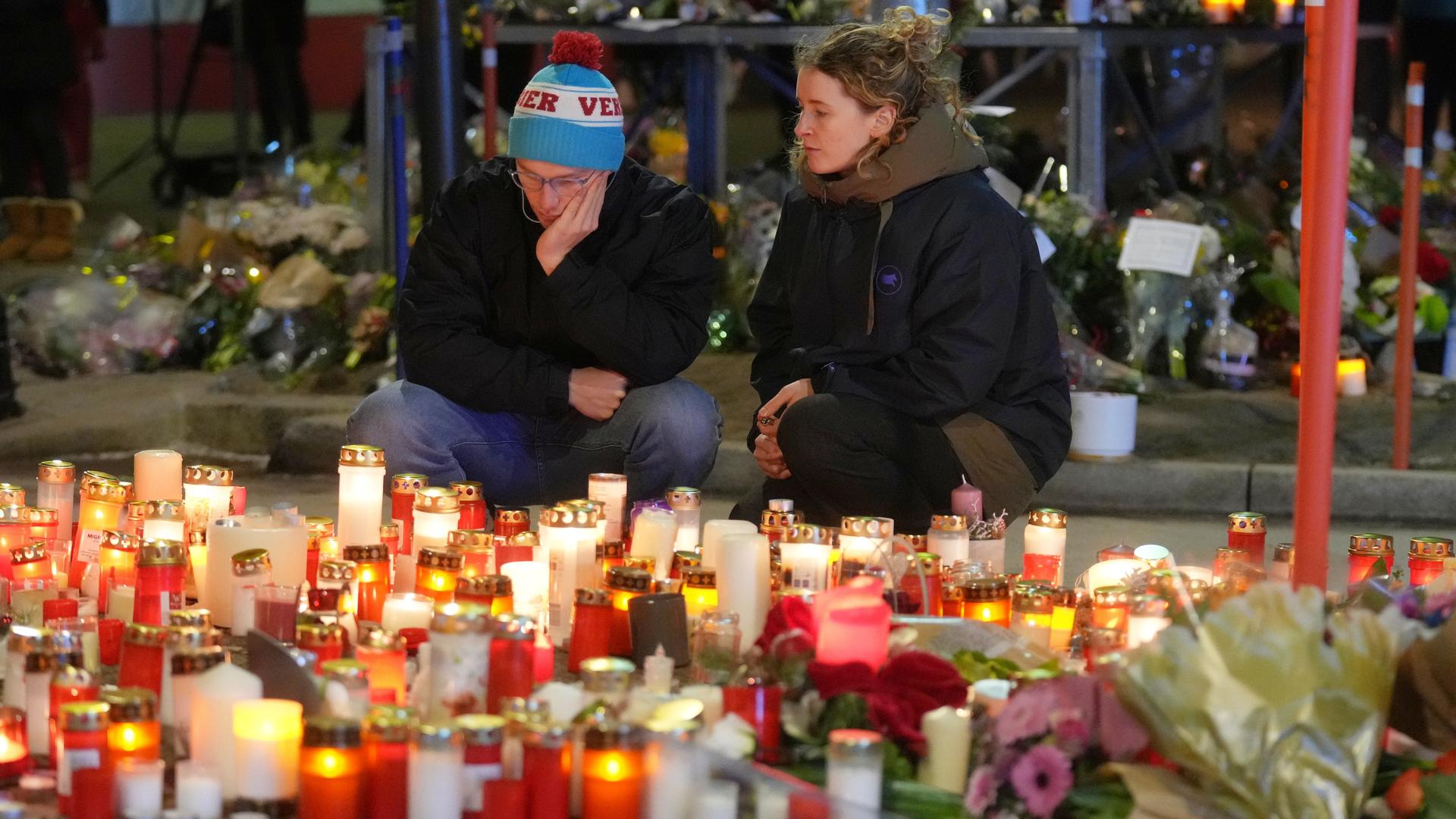 Ein Mann und eine Frau sitzen traurig vor vielen Kerzen und Blumen. Ein Mann und eine Frau sitzen traurig vor vielen Kerzen und Blumen.
