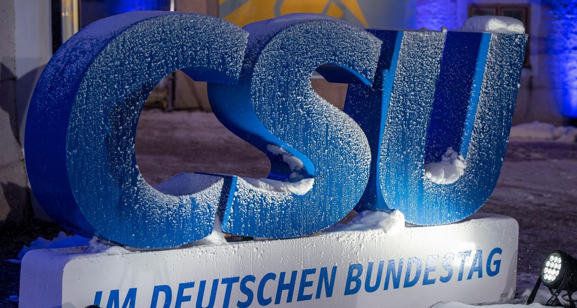 Auf einem draußen aufgestellten, großen, blauen Logo der CSU liegt Schnee.