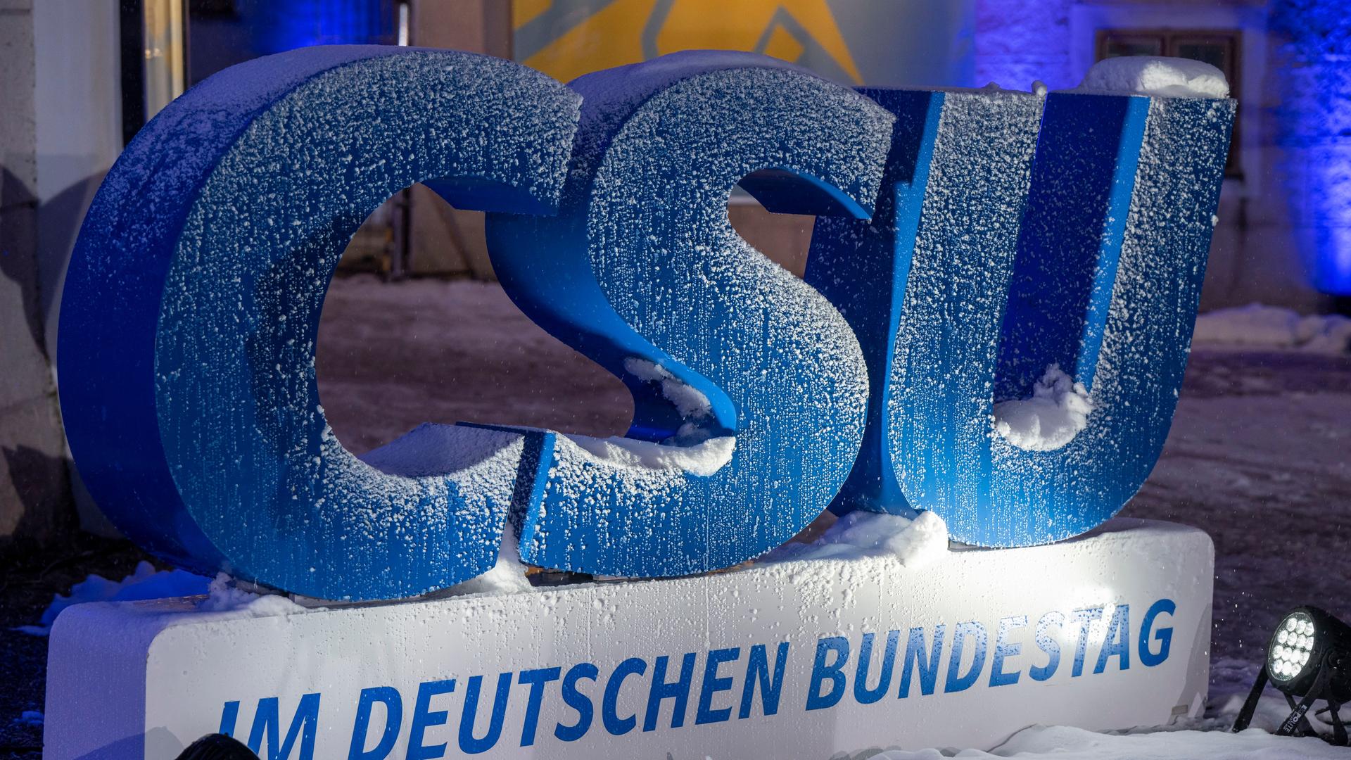 Auf einem draußen aufgestellten, großen, blauen Logo der CSU liegt Schnee.
