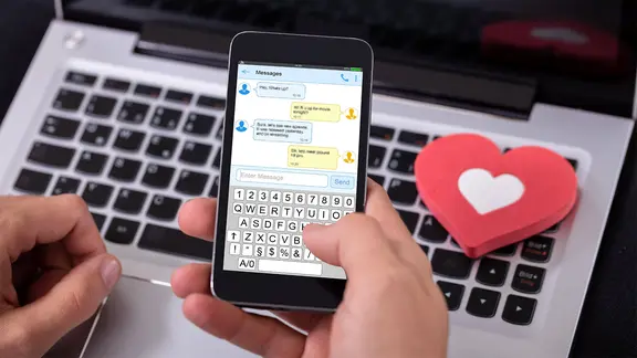 Eine Hand hält ein Handy mit einem offenen Chatverlauf.