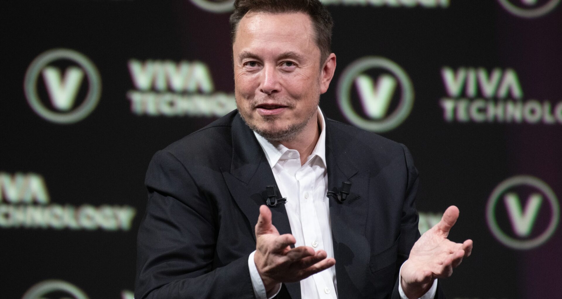 Elon Musk zeigt mit seinen Händen, warum er vielleicht in Bitcoin investieren wird.