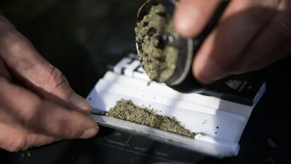 Ein Mann schüttet zerkleinertes Marihuana in einen Joint. 