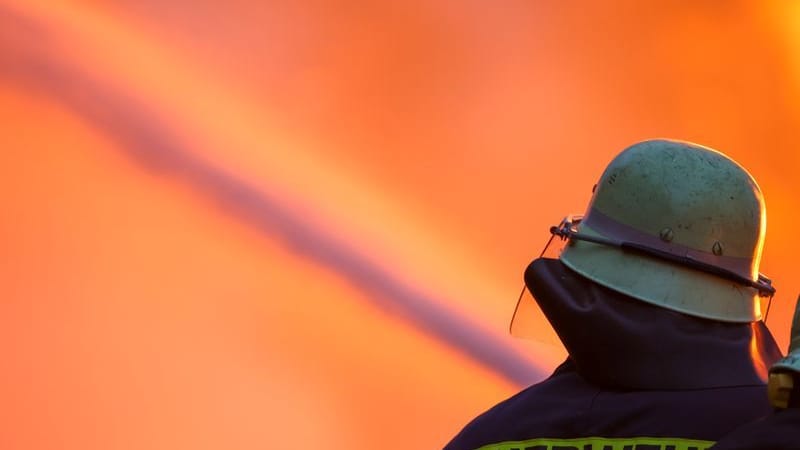 Ein Feuerwehrmann löscht ein Feuer (Symbolbild); Durch den Rauch eines Grills in einer Wohnung wurden drei Menschen schwer verletzt.