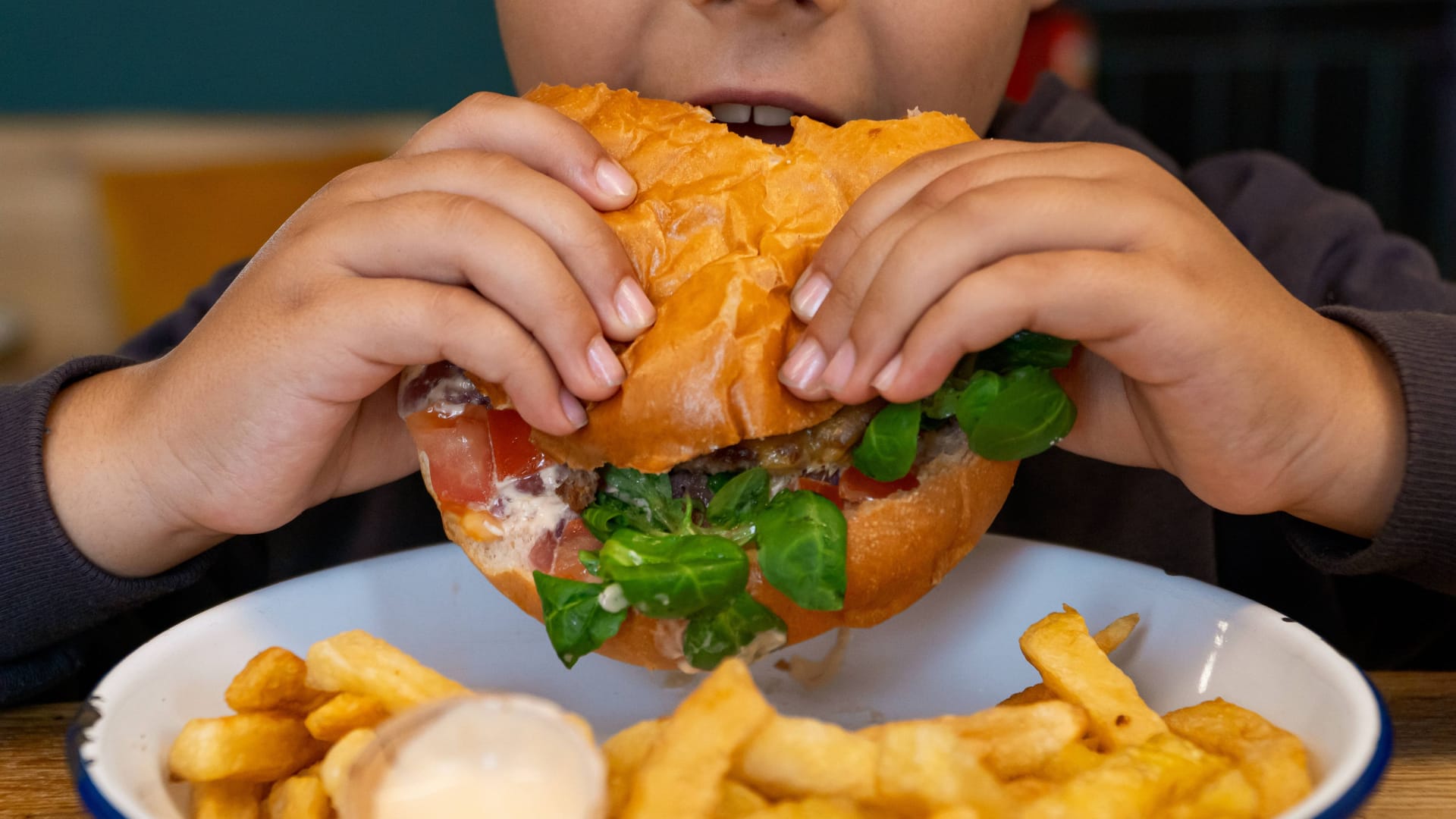 Ein Kind beißt in einen Burger (Symbolbild): Die Stadt mit der höchsten Dichte an Fast-Food-Restaurants in Deutschland pro 100.000 Einwohner liegt in Bayern. Ein Kind beißt in einen Burger (Symbolbild): Die Stadt mit der höchsten Dichte an Fast-Food-Restaurants in Deutschland pro 100.000 Einwohner liegt in Bayern.
