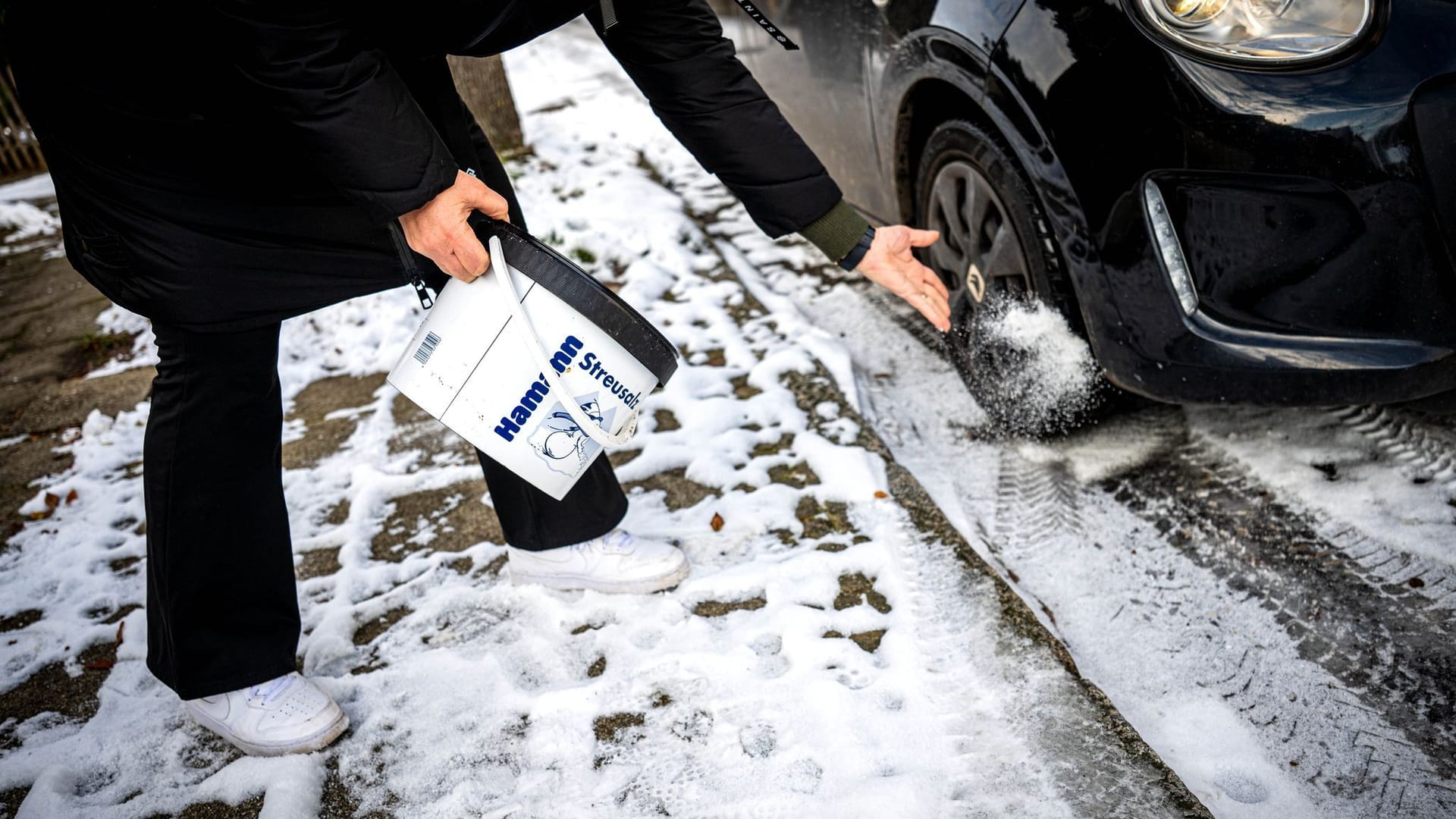 Eine Frau streut Salz vor ihr Auto (Symbolbild): Die Nachfrage nach Taumitteln in den großen Hamburger Baumarktketten ist groß.
