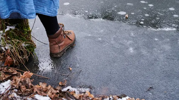 Eine Person betritt eine zugefrorene Eisfläche.
