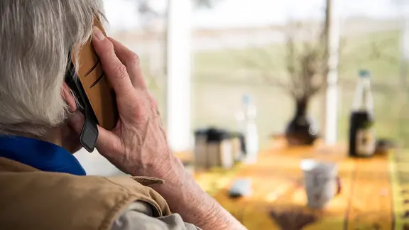 Senior schaut aus dem Fenster während eines Telefonats