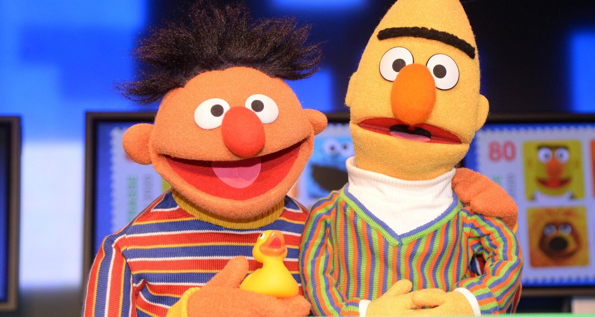 Die Puppen Ernie & Bert aus der Sesamstraße. Ernie hat ein Quietscheentchen in der Hand und seien Arm um Bert gelegt