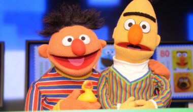 Die Puppen Ernie & Bert aus der Sesamstraße. Ernie hat ein Quietscheentchen in der Hand und seien Arm um Bert gelegt