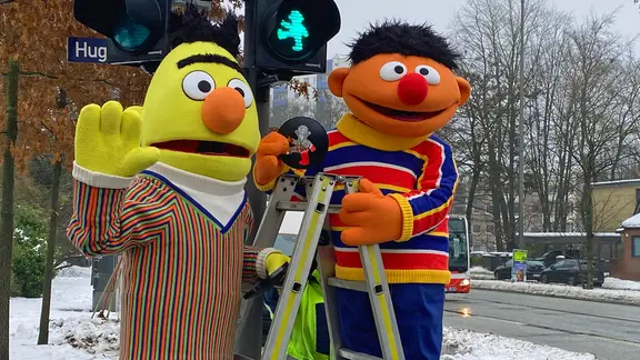 Ernie und Bert stehen vor einer Ampel auf einer Leiter