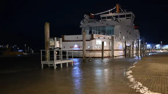 Das Wasser ist im Hafen von Norddeich über die Kaimauer gelaufen, die Norderney -Fähre liegt sicher vertaut. | picture alliance/dpa | Lars Penning Das Wasser ist im Hafen von Norddeich über die Kaimauer gelaufen, die Norderney -Fähre liegt sicher vertaut.