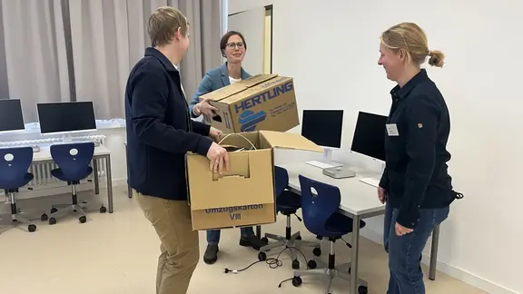 Zwei Frauen und ein Mann tragen Kartons.