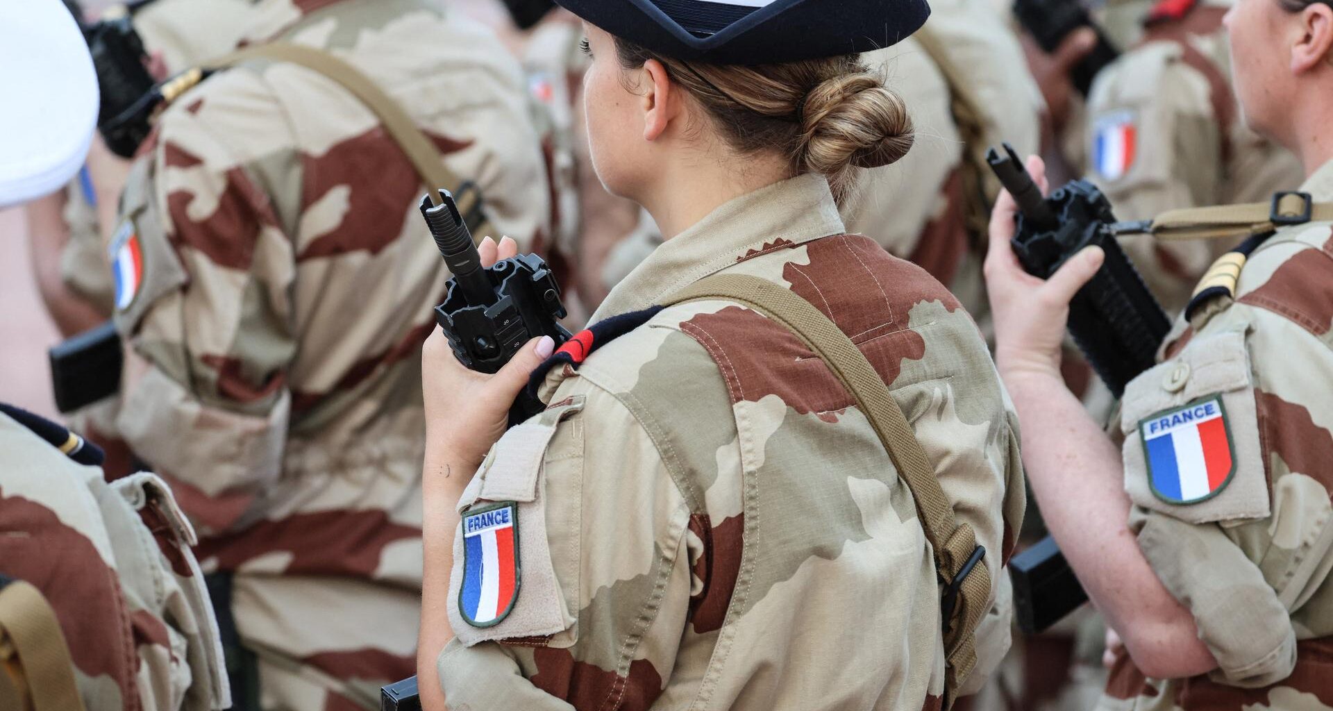 Eine Soldatin hält ein Gewehr vor der Brust, auf ihrem Hemdarm sieht man die französische Fahne.