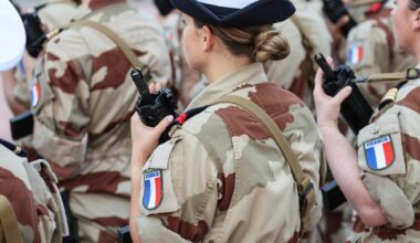 Eine Soldatin hält ein Gewehr vor der Brust, auf ihrem Hemdarm sieht man die französische Fahne.