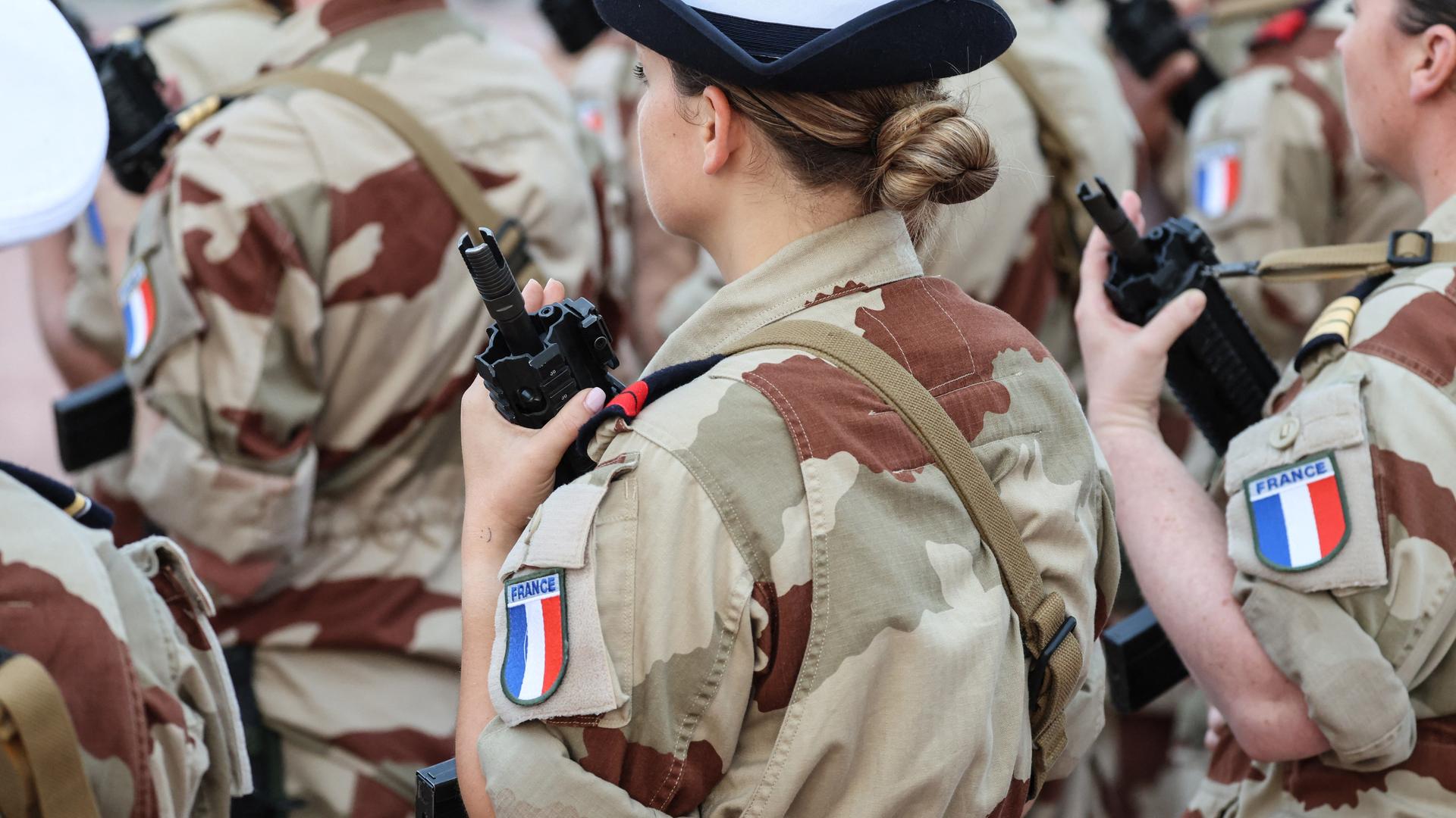 Eine Soldatin hält ein Gewehr vor der Brust, auf ihrem Hemdarm sieht man die französische Fahne.