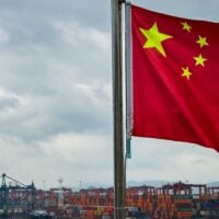 SHENZHEN, CHINA - APRIL 12: A Chinese national flag is seen in the foreground with container ships, cranes, and stacked shipping containers at the Yantian International Container Terminal under cloudy skies, on April 12, 2025 in Shenzhen, China. China has imposed a new round of retaliatory tariffs on U.S. imports, raising duties to 125% in response to the latest escalation by the United States, which increased tariffs on Chinese goods to 145%. The growing trade tensions have further impacted China's export sector, affecting key industries such as logistics, manufacturing, and cross-border e-commerce. The measures are part of Beijing's broader strategy to counter rising economic pressure and defend its trade interests. (Photo by Cheng Xin/Getty Images)