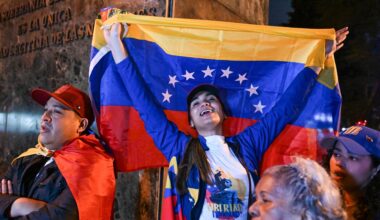 Eine Frau reißt eine venezolanische Nationalflagge in die Höhe. Sie steht zwischen weiteren Teilnehmern einer spontanen Versammlung von Exil-Venezolanern.