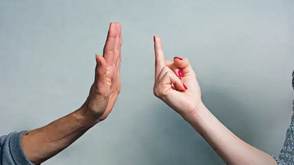 Eine weibliche Hand zeigt den Mittelfinger, eine männliche Hand macht eine abwehrende Geste.