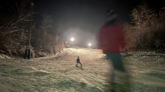 Skifahrer fahren abends bei Flutlicht eine Skihang herunter. | NDR, Jan Fragel Skifahrer fahren abends bei Flutlicht eine Skihang herunter.