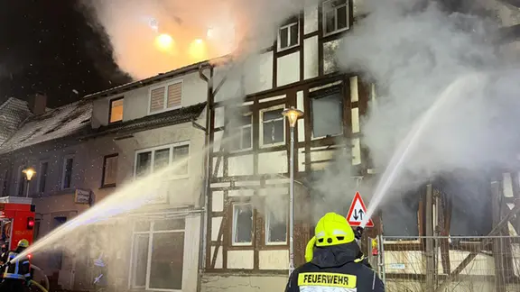 Zwei Feuerwehrleute löschen ein Fachwerkhaus. Aus dem Dach schlagen Flammen. | Kreisfeuerwehr Holzminden Zwei Feuerwehrleute löschen ein Fachwerkhaus. Aus dem Dach schlagen Flammen.