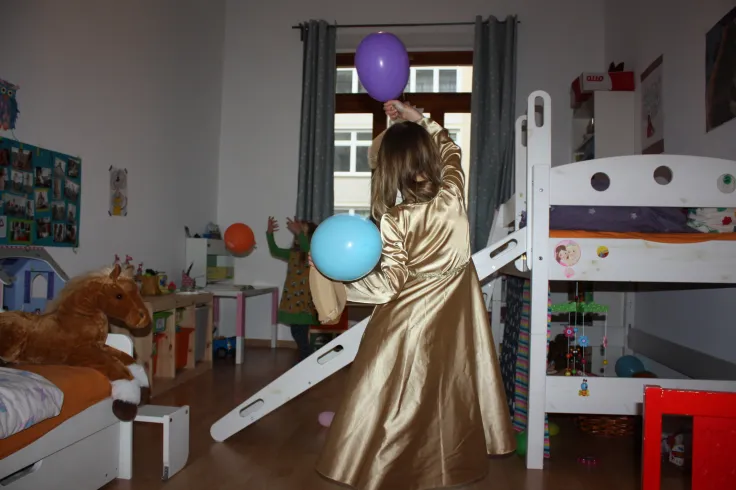 Kind mit zwei Luftballon und im goldenen Kleid im Kinderzimmer
