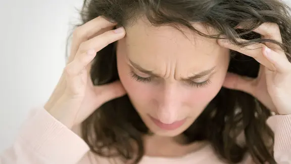 Eine Frau mittleren Alters stützt ihren Kopf mit den Händen und schaut zu Boden.