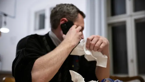 Ein Mann hält ein Taschentuch in einer Hand und ein Telefon in der Anderen.