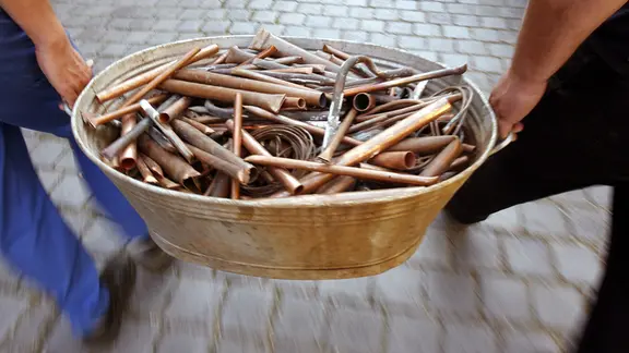 Zwei Personen tragen eine mit Kupferrohren gefüllte Zinkwanne | picture-alliance/ ZB Zwei Personen tragen eine mit Kupferrohren gefüllte Zinkwanne