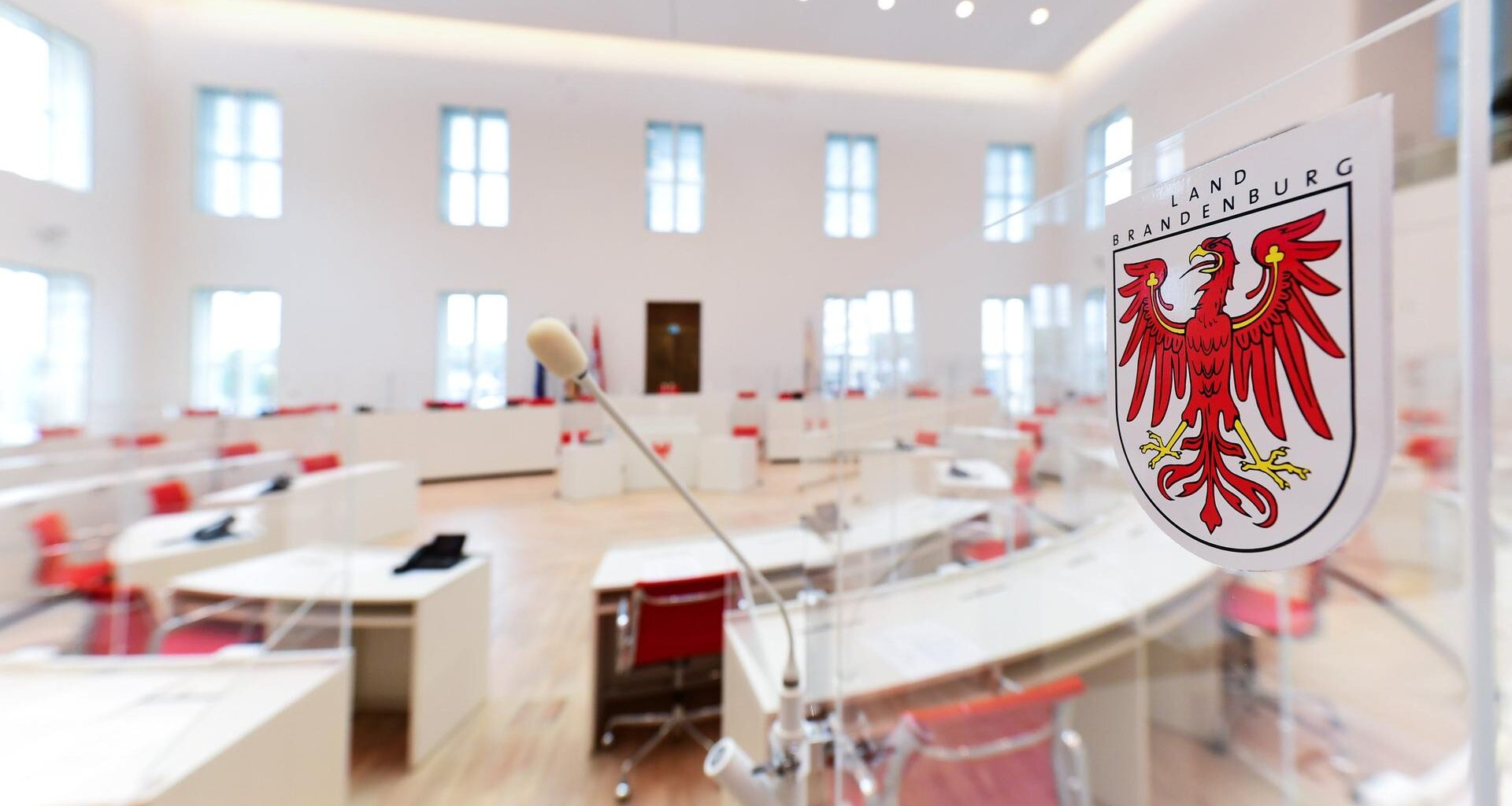 Blick in den Brandenburger Landtag. Weiße, in einem Rund angeordnete Tische sind zu sehen. Rote Sessel stehen an den Tischen.