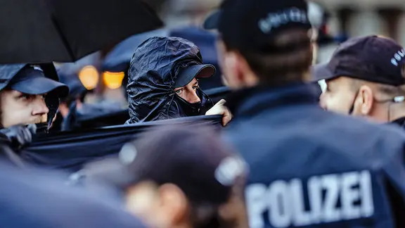 Polizisten und vermummte Demonstranten stehen sich bei einer Demo gegenüber.