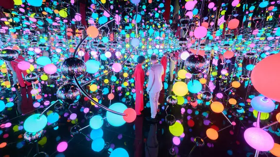 Zwei Personen stehen in einem Ausstellungsraum voller Spiegel und Lichter. 