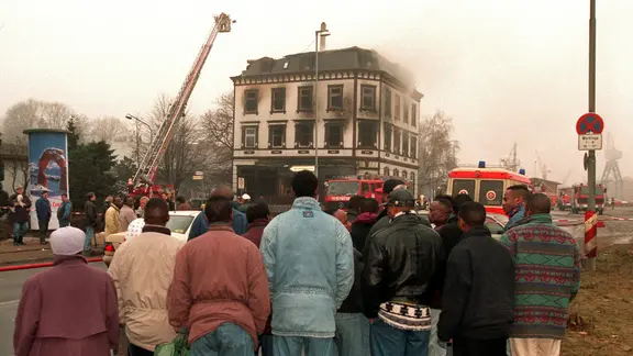 Menschen stehen 19. Januar 1996 vor der Ruine der ausgebrannten Flüchtlingsunterkunft in Lübeck.