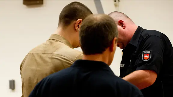 Der verurteilte Straftäter Alexander K. steht hinter zwei Justizbeamten.