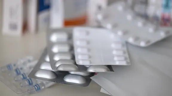 Mehrere Packungen mit Tabletten, Pflastern und Tropfen liegen auf einem Tisch.