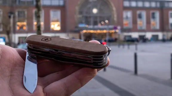 Vor dem Hauptbahnhof Kiel wird ein Taschenmesser in der Hand gehalten.