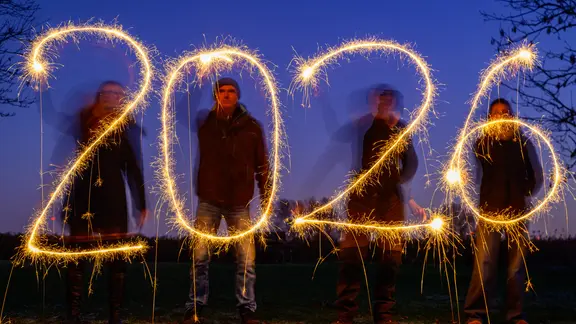 Vier Menschen zeichnen mit Wunderkerzen die Jahreszahl 2026 in den abendlichen Himmel.
