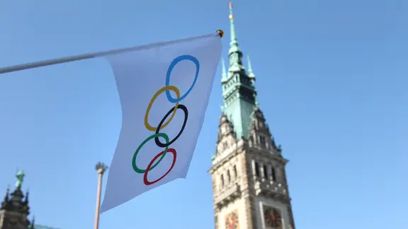 Eine Flagge mit den olympischen Ringen hängt an einem Laternenpfahl vor dem Hamburger Rathaus. | IMAGO / Hanno Bode Eine Flagge mit den olympischen Ringen hängt an einem Laternenpfahl vor dem Hamburger Rathaus.