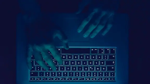 Zwei Hände über einer Tastatur im Dunklen.