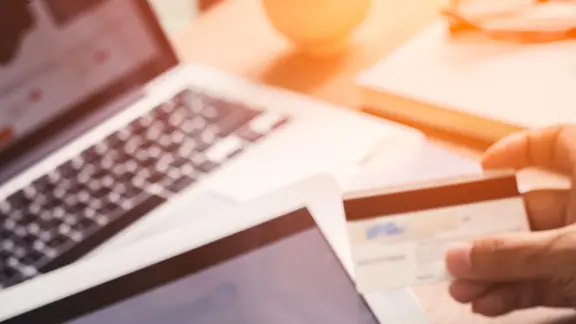 Eine Person hält eine Kreditkarte vor einen Laptop