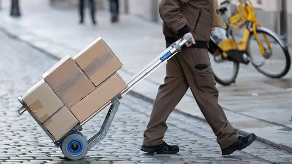 Der 29-Jährige liefert laut Polizei Pakete für einen Online-Versandhandel aus. (Themenbild) | picture alliance/dpa | Sebastian Kahnert Ein Paketzusteller zieht mit einem Gerät mehrere Pakete über eine Straße.