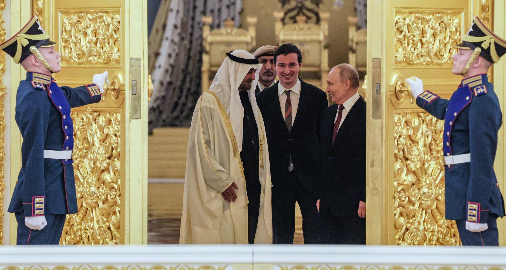 Der russische Präsident Putin und der Präsident der Vereinigten Arabischen Emirate, Scheich Mohamed bin Zayed Al Nahyan, stehen sich gegenüber und schauen sich an. Ihnen wird von zwei Soldaten eine goldbesetzte Tür aufgehalten.