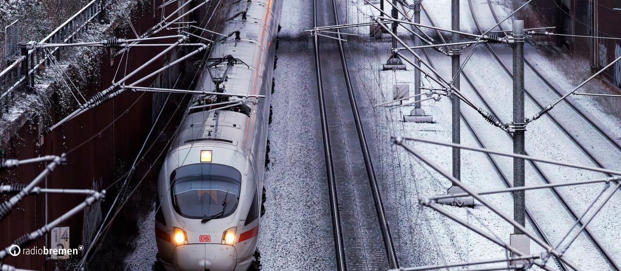 Ein Zug fährt über Gleise, die mit Schnee bedeckt sind.