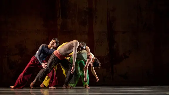 Tanzende Männer lehnen sich auf einer Bühne in die gleiche Richtung. 