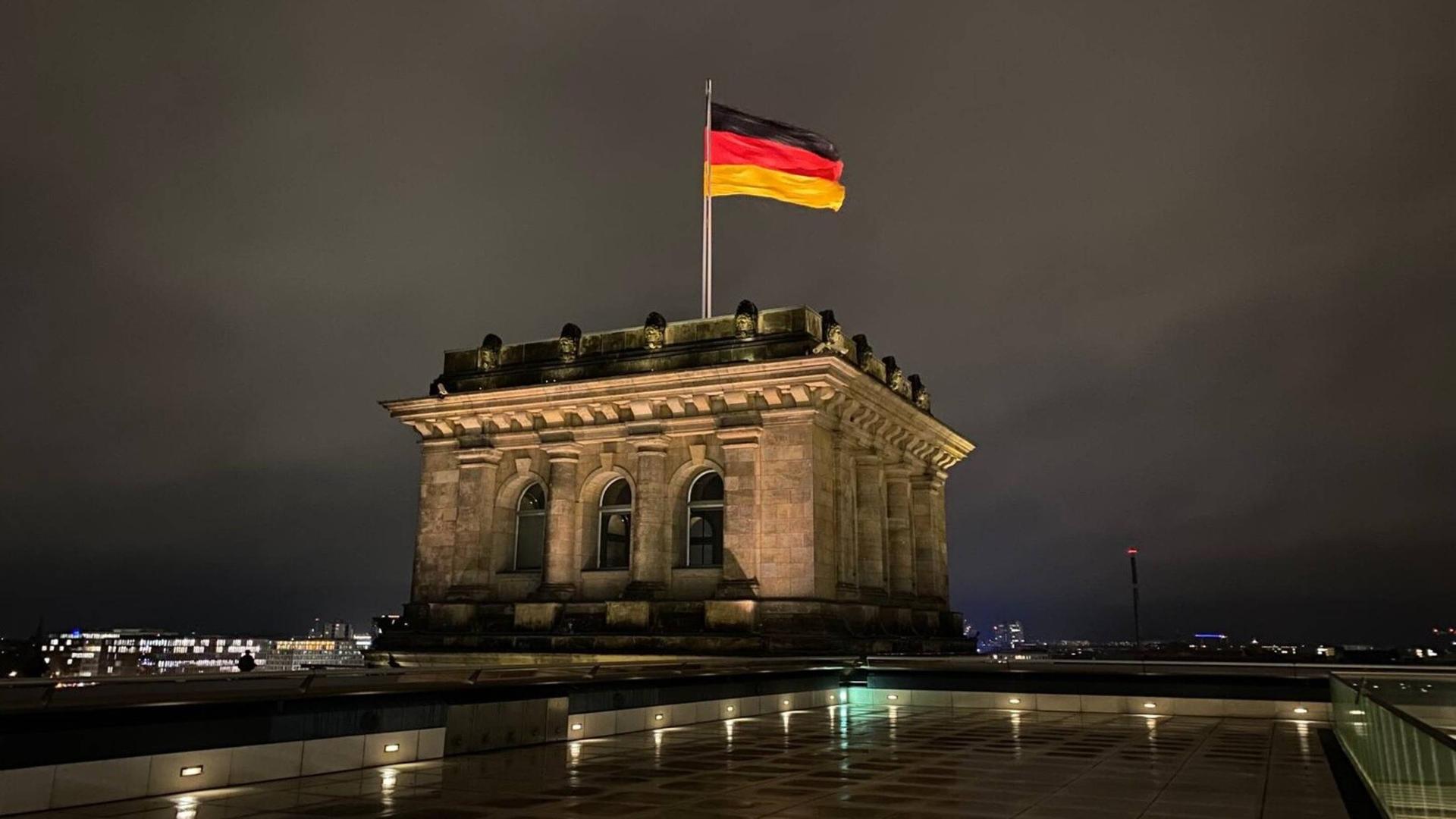 Die Deutschlandfahne auf dem Dach des Reichstages bei Nacht.