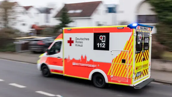 Ein Rettungswagen des Deutschen Roten Kreuzes fährt mit eingeschaltetem Blaulicht durch eine Straße.