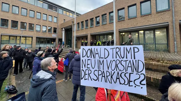 "Donald Trump neu im Vorstand der Sparkasse?" steht auf einem Protestschild | NDR, Jan Fragel "Donald Trump neu im Vorstand der Sparkasse?" steht auf einem Protestschild